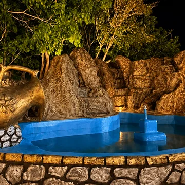 استخر رو‌باز با آبنمای سنگی و کوزهٔ برنجی، در نور شب